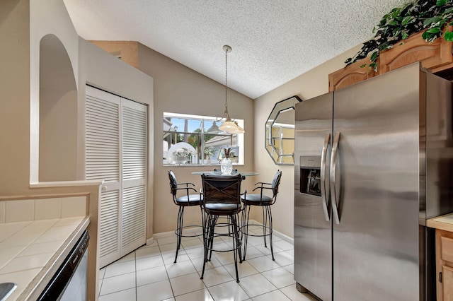 kitchen with vaulted ceiling, light tile patterned floors, pendant lighting, stainless steel appliances, and tile countertops