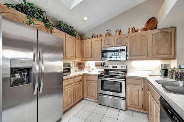 kitchen featuring vaulted ceiling with skylight, light tile patterned floors, a textured ceiling, stainless steel appliances, and light brown cabinetry