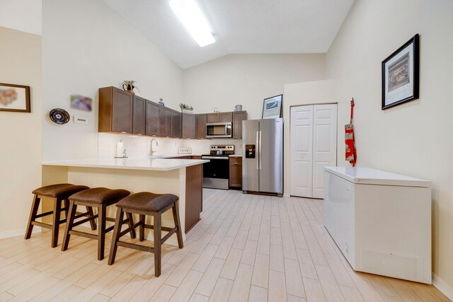 kitchen featuring a kitchen breakfast bar, light hardwood / wood-style floors, kitchen peninsula, and appliances with stainless steel finishes