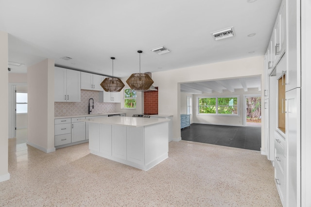 kitchen with white cabinets, backsplash, a kitchen island, decorative light fixtures, and sink