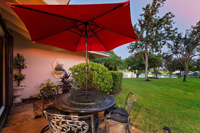 patio terrace at dusk featuring a water view and a lawn