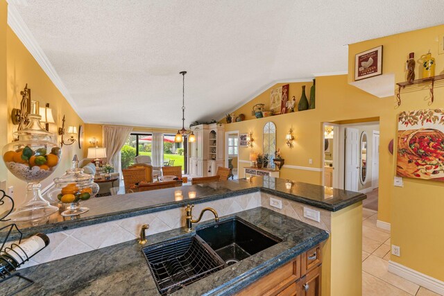 kitchen with light tile patterned floors, sink, a textured ceiling, crown molding, and vaulted ceiling