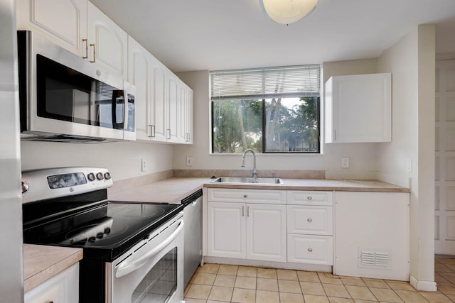 kitchen featuring appliances with stainless steel finishes, sink, light tile patterned floors, and white cabinets