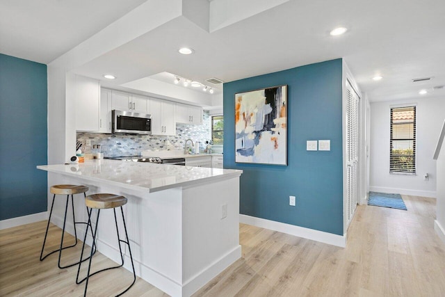 kitchen featuring light hardwood / wood-style floors, white cabinetry, backsplash, kitchen peninsula, and sink