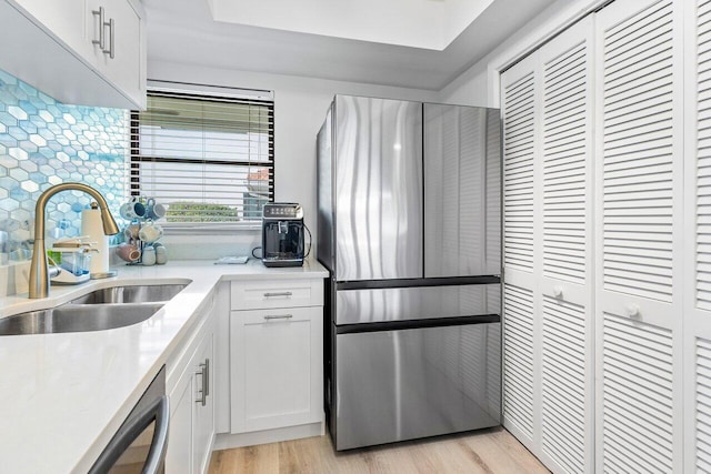 kitchen with light wood-type flooring, sink, white cabinets, stainless steel appliances, and backsplash