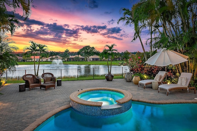 pool at dusk with a patio, an in ground hot tub, and a water view