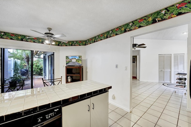 kitchen with a textured ceiling, white cabinets, tile counters, and light tile patterned floors