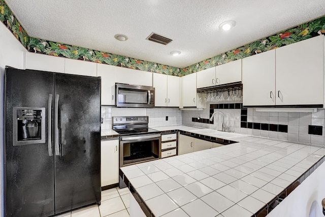 kitchen featuring sink, appliances with stainless steel finishes, tile counters, and white cabinetry