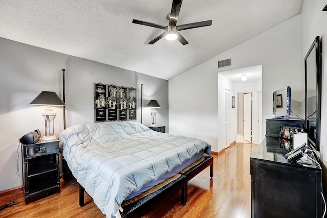 bedroom with hardwood / wood-style floors, a textured ceiling, vaulted ceiling, and ceiling fan