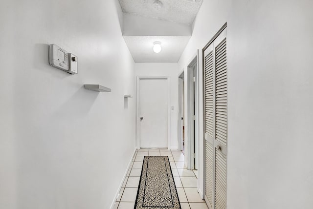 corridor with lofted ceiling, a textured ceiling, and light tile patterned floors