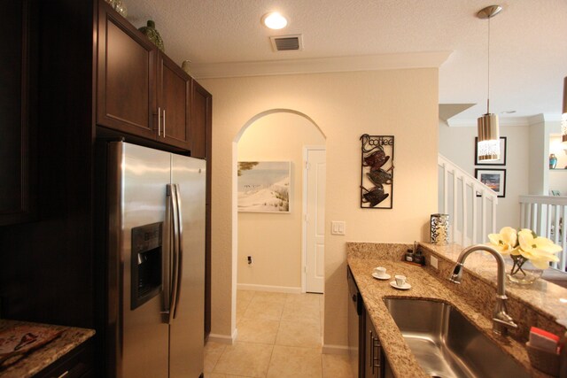 kitchen with sink, ornamental molding, stainless steel refrigerator with ice dispenser, hanging light fixtures, and light stone countertops