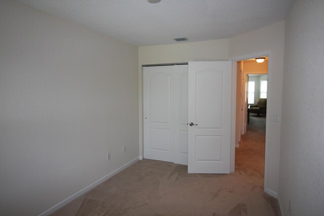 unfurnished bedroom with light carpet and a closet