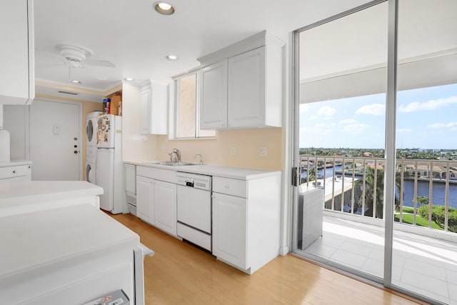 kitchen with white cabinets, light hardwood / wood-style flooring, stacked washer / drying machine, and white appliances