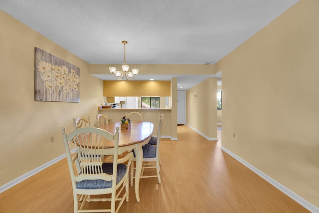 dining space featuring wood finished floors, a chandelier, a textured ceiling, and baseboards
