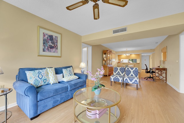 living room with a textured ceiling, ceiling fan, and light hardwood / wood-style flooring