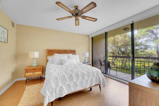 bedroom featuring multiple windows, access to exterior, wood finished floors, floor to ceiling windows, and a textured ceiling