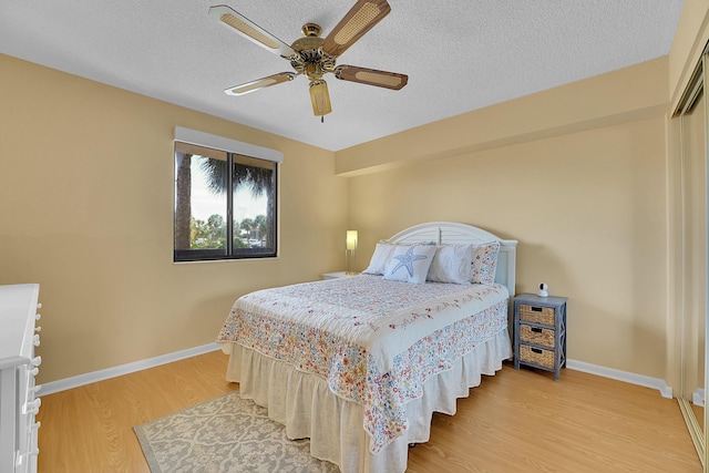 bedroom featuring light wood-style flooring, baseboards, a textured ceiling, and a ceiling fan