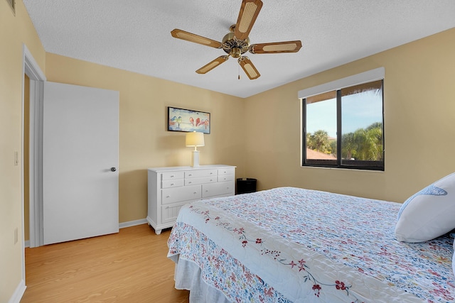 bedroom with light wood-type flooring, a textured ceiling, baseboards, and a ceiling fan
