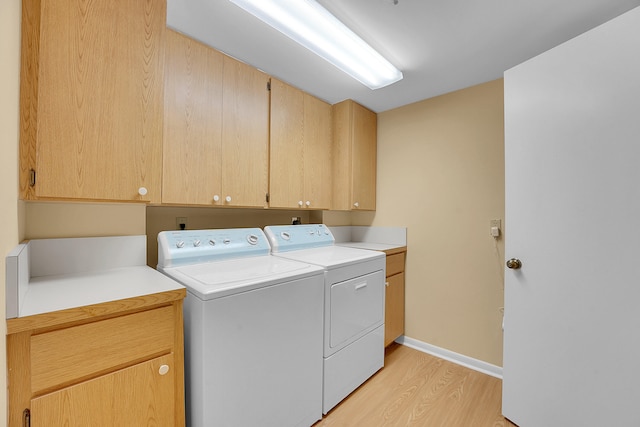 laundry area with washing machine and clothes dryer, light hardwood / wood-style floors, and cabinets