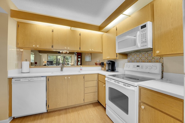 kitchen with white appliances, a sink, light countertops, light wood finished floors, and tasteful backsplash