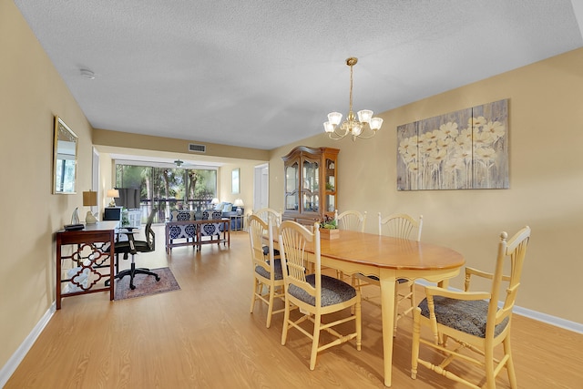 dining room with an inviting chandelier, light wood-type flooring, and a textured ceiling