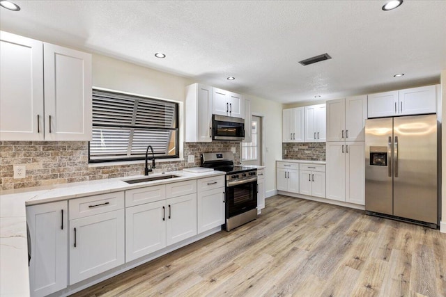 kitchen with sink, light hardwood / wood-style flooring, appliances with stainless steel finishes, tasteful backsplash, and white cabinetry