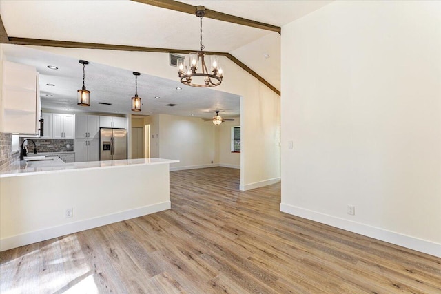 kitchen with sink, hanging light fixtures, vaulted ceiling with beams, stainless steel refrigerator with ice dispenser, and white cabinets