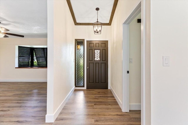 foyer with crown molding, wood-type flooring, and ceiling fan with notable chandelier