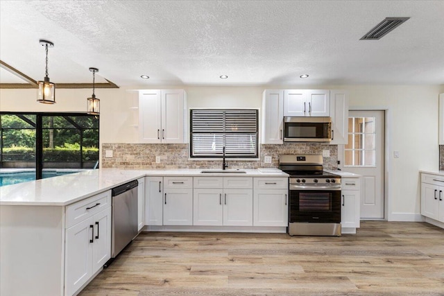 kitchen featuring sink, hanging light fixtures, stainless steel appliances, kitchen peninsula, and white cabinets