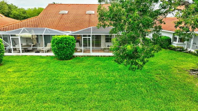 rear view of house featuring a yard, glass enclosure, and a patio