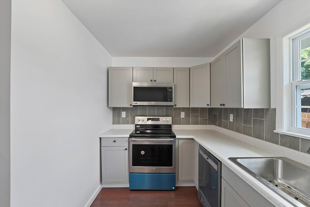 kitchen with gray cabinets, dark hardwood / wood-style floors, sink, stainless steel appliances, and backsplash