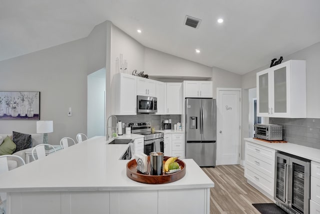 kitchen with lofted ceiling, white cabinets, beverage cooler, stainless steel appliances, and light hardwood / wood-style flooring