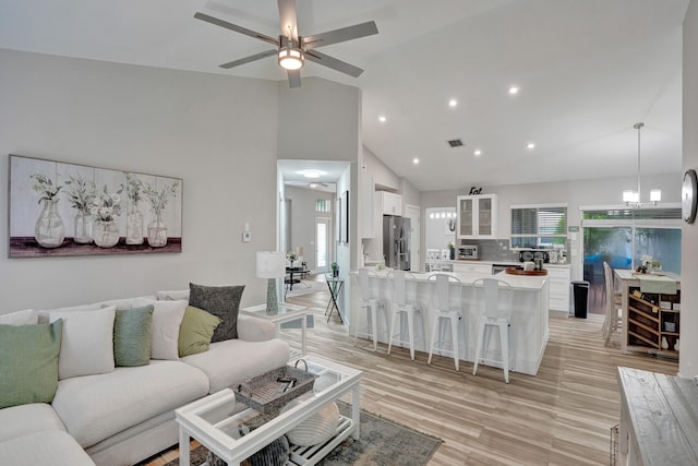 living room with high vaulted ceiling, ceiling fan with notable chandelier, plenty of natural light, and light hardwood / wood-style floors