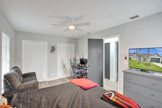 bedroom with ceiling fan, light hardwood / wood-style flooring, and multiple closets