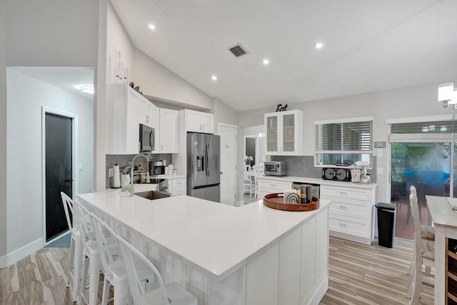 kitchen with white cabinetry, vaulted ceiling, a kitchen breakfast bar, stainless steel appliances, and light hardwood / wood-style floors