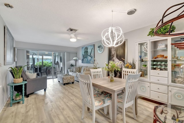 dining area with ceiling fan with notable chandelier, light wood-type flooring, and a textured ceiling