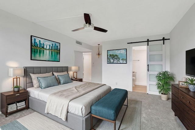 carpeted bedroom featuring ensuite bathroom, a barn door, and ceiling fan