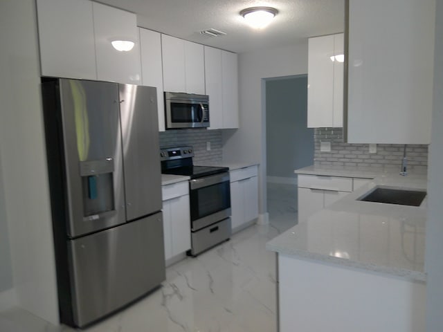 kitchen featuring white cabinets, sink, tasteful backsplash, stainless steel appliances, and light stone countertops