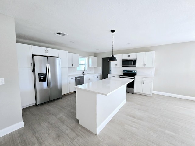 kitchen with sink, white cabinetry, a kitchen island, appliances with stainless steel finishes, and decorative light fixtures