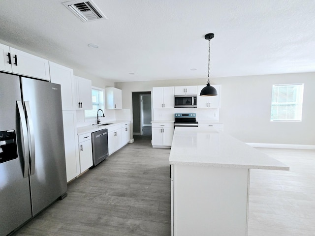 kitchen featuring white cabinets, a center island, appliances with stainless steel finishes, and hanging light fixtures