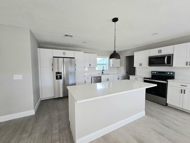 kitchen with appliances with stainless steel finishes, light hardwood / wood-style floors, white cabinets, a kitchen island, and pendant lighting