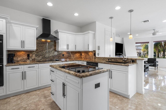 kitchen featuring ceiling fan, a center island, wall chimney exhaust hood, sink, and black appliances