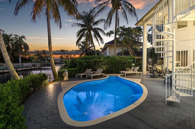 pool at dusk with a water view and a patio