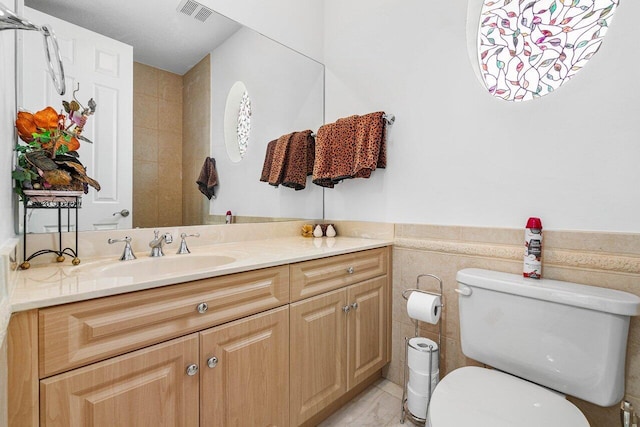 bathroom with vanity, toilet, and tile walls