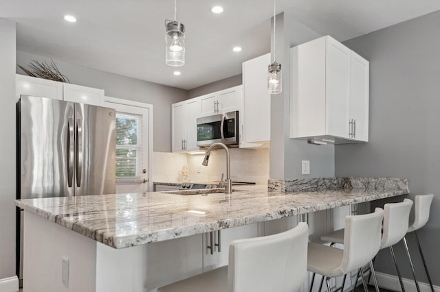 kitchen featuring light stone counters, a peninsula, white cabinetry, appliances with stainless steel finishes, and backsplash