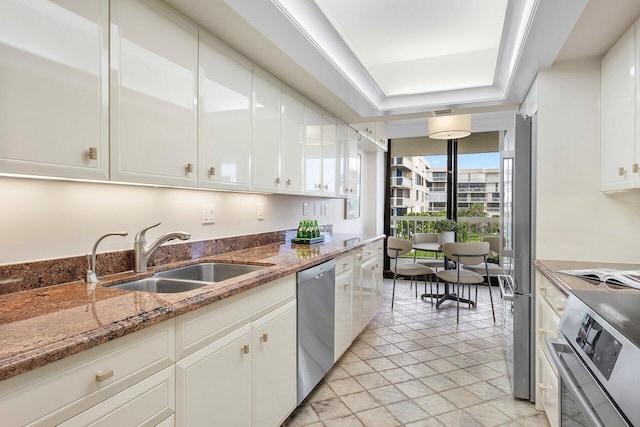 kitchen with stainless steel appliances, sink, stone countertops, a wall of windows, and white cabinets