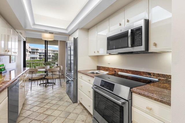 kitchen with dark stone counters, a raised ceiling, white cabinetry, a wall of windows, and stainless steel appliances