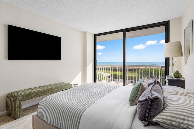 tiled bedroom with access to exterior, a water view, a textured ceiling, and expansive windows