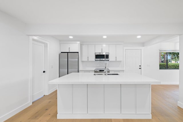 kitchen with a center island with sink, light hardwood / wood-style floors, stainless steel appliances, and white cabinets