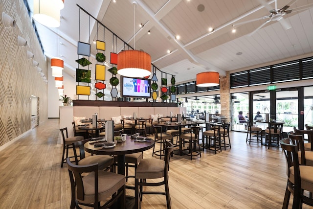 dining space featuring light hardwood / wood-style floors, beamed ceiling, wooden ceiling, a high ceiling, and ceiling fan